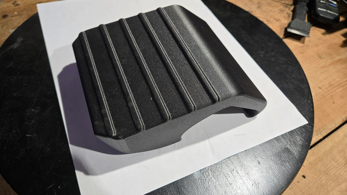 Black 3D-printed snap-on sidestep accessory with textured grip, displayed on a table.